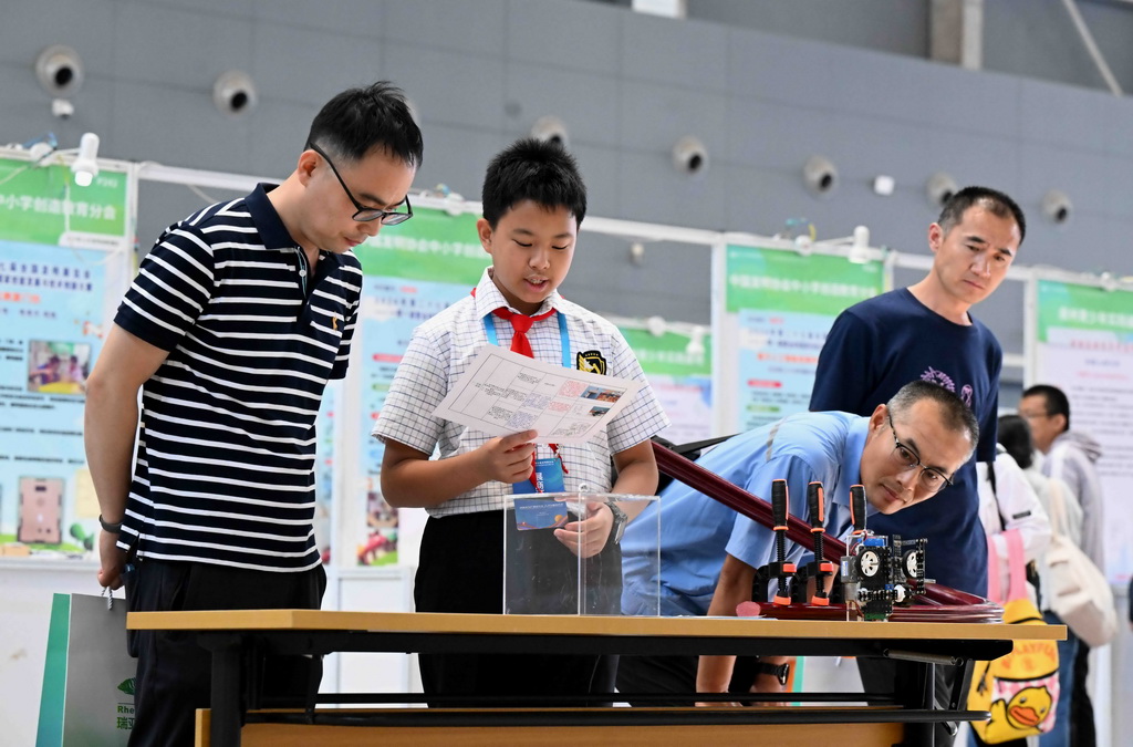 5月22日，在第27届全国发明展览会现场，一名小朋友（左二）介绍自己的发明创造情况。新华社发（陈其保摄）